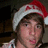 A pixelated image shows a person wearing a red and white Santa hat with 'MERRY' visible, against a solid red background with yellow text reading 'Alex Gaskarth Is Sex No?'.