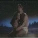 Static pixelated image of two figures in a close embrace on a dark background with blue and purple lighting effects.
