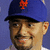 A pixelated image of a person wearing a blue cap with an orange NY logo, smiling against a purple background.