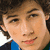 Pixelated close-up of a person with brown hair, light skin, and a blue garment, smiling with visible teeth.
