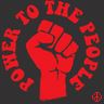 Static red icon on dark background featuring raised fist surrounded by circular text "POWER TO THE PEOPLE" with peace symbol in bottom right corner.