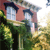 Pixelated static image of a two-story house with pinkish-red walls, dark blue roof, and white-framed windows, surrounded by green foliage and yellowish ground cover.