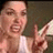 A pixelated close-up of a person with light skin tone wearing a white shirt, holding a white object near their face.