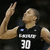 Pixelated image of a person in a dark jersey with white text and number 30, raising one arm against a dark background.