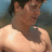 Pixelated image of a shirtless person with dark hair and a visible tattoo on the upper back, surrounded by pink text on a black background.