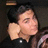 Pixelated close-up of a person with light skin and dark hair, wearing a black top with white accents against a dark background.