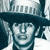 Pixelated image of a person wearing a dark wide-brimmed hat with a light-colored band, standing against a blurred background with vertical lines.