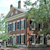 Pixelated static image of a two-story building with brown trim, blue windows, and a tree to the right under a light blue sky.