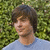 Pixelated image of a person with brown hair wearing a light blue shirt against a green foliage background.