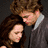 Two people in a close embrace, one in dark clothing leaning toward the other in a light shirt, with a blurred outdoor background.