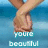 Pixelated image of a person's lower legs and feet standing in shallow blue water with text reading 'you're beautiful' below.