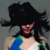 A pixelated figure with long dark hair wears a large black hat and a sleeveless top with blue and green sections against a gray background.