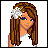 Pixelated image of a character with long brown hair, white flower accessory, green eyes, and purple eyeshadow wearing white top.