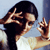 Static pixelated image of a person with dark hair wearing a white top, making hand gestures near their face against a light blue background.