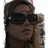 Pixelated close-up of a person with dark hair wearing large black sunglasses and holding an object near their face.