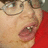 A person wearing glasses and a red shirt with mouth open showing teeth in four