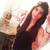 A pixelated image of a person with long dark hair wearing a sleeveless top, holding an object near their face against a light background.