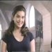 Static 75x75 pixel image of a woman with long dark hair wearing a black top, positioned against an indoor background with light-colored walls and vertical architectural elements.