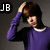 Pixelated image of a person in a purple long-sleeve shirt with white collar, hand raised to head, dark hair, and 'JB' text in black square on left.