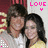 Two people in close pose with one person's arm around the other, wearing white and yellow tops against a red background with partial text.