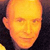 A static pixelated image of a bald human head with closed eyes, rendered in warm orange and yellow tones against a dark background.