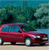 A red sedan with blue-tinted windows sits on a light-colored surface against a blurred green and blue background.