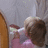 Pixelated image of a person with brown hair in a bun wearing pink clothing, holding an object near their face against a gray background.