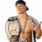 A shirtless man with dark hair wears a championship belt and holds a microphone, with pink text overlaid on the right side.