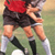 Pixelated static image of a person in sports attire holding an object, likely a soccer ball, on a grassy field background.