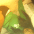 Green-shirted figure with white emblem on chest, light-colored sleeves, and orange background elements in a static image.