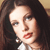 Pixelated close-up of a person with long dark hair, light skin, and red lips wearing a white top with a dark collar.