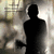 Silhouette of a standing figure with arms at sides against a blurred background of light and dark tones.