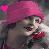 Pixelated image of a person with pink hair wearing dark clothing and holding a red object, set against a blurred background.