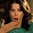 Pixelated static image of a person with long dark hair, light skin tone, and open mouth expression holding an object near their face.