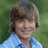 A pixelated image of a person with brown hair in a blue checkered shirt against a green background, with pink text on a cyan background.