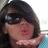 A pixelated image of a person with dark hair and sunglasses blowing a kiss, set against a bright blue background with yellow text.