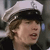 A pixelated close-up of a person wearing a white sailor cap with a black band, brown hair, and a dark shirt, with a blurred background.