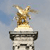 A pixelated statue of a winged horse on a stone pedestal against a light blue sky background.