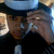 A person wearing a dark jacket and light blue cap holds a clear glass to their mouth in three showing slight movement