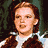 Pixelated image of a person with brown hair wearing a white shirt and brown vest against dark background, next to blue with pixelated text