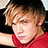 Pixelated image of a person with light brown hair wearing red clothing, set against yellow background with green text.