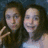 Two identical figures with long brown hair and light skin pose side-by-side against a dark blue background, one making a peace sign while the other smiles.