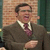 Static pixelated image of a man in business attire against a brick wall background with green vertical element.
