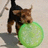 A pixelated dog with brown and black fur holds a large green ball in its mouth against a light background.