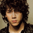 Pixelated static image of a person with dark curly hair, light skin tone, and closed eyes wearing a black jacket over a white shirt against a beige background.