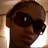Pixelated close-up of a person's face wearing dark sunglasses with reflective highlights, set against a light brown background.