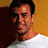 Static 48x48 pixel icon showing a close-up of a person's face with dark hair and light skin, wearing a white shirt against an orange-brown background.