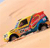 A pixelated, colorful car icon with red, blue, yellow, and green hues on a light peach background, angled diagonally from left to right.