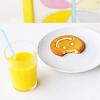 A glass of yellow liquid with a light blue straw sits next to a white plate holding a golden-brown pastry with a spiral pattern and a bite taken out of it.