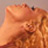 Pixelated static image of a light brown or orange-toned figure with indistinct facial features and hair, set against a muted background.